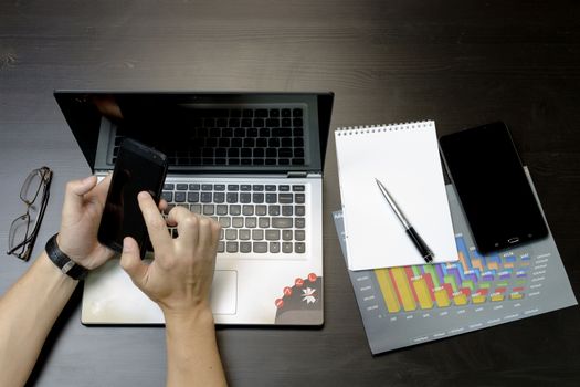 Businessman working on an ultra-thin laptop. Nearby are a block, a marker, a pen, glasses, a tablet phone. On his hand is an expensive watch.