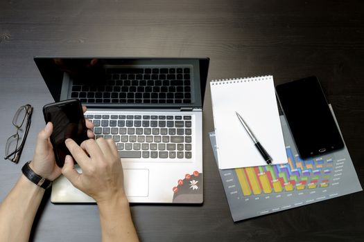 Businessman working on an ultra-thin laptop. Nearby are a block, a marker, a pen, glasses, a tablet phone. On his hand is an expensive watch.