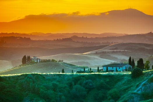 Evening in Tuscany. Hilly Tuscan landscape in golden mood at sunset time with silhouettes of cypresses and farm houses, Italy.