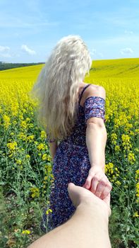 blonde girl in dress with flower print on the blooming yellow rapeseed field