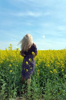 blonde girl in dress with flower print on the blooming yellow rapeseed field