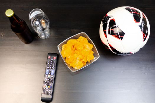 People prepared to watch football on TV with beer. There's beer on the table, ball, TV remote, snacks. Craft beer. Light background. The view from the top.