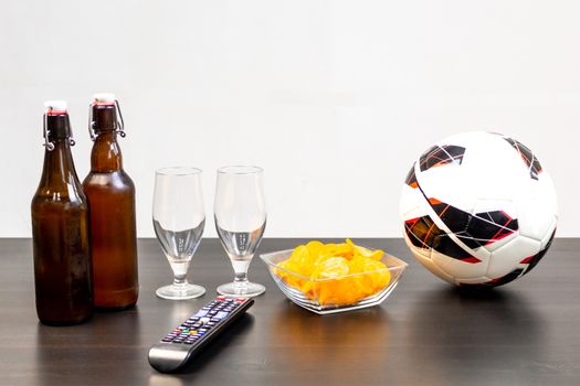 People prepared to watch football on TV with beer. There's beer on the table, ball, TV remote, snacks. Craft beer. Light background.