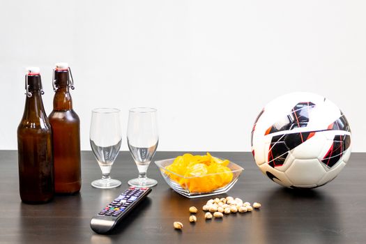 People prepared to watch football on TV with beer. There's beer on the table, ball, TV remote, snacks. Craft beer. Light background.