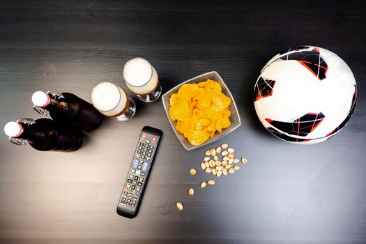 People prepared to watch football on TV with beer. There's beer on the table, ball, TV remote, snacks. Craft beer. Light background. The view from the top.