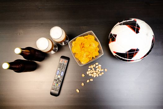 People prepared to watch football on TV with beer. There's beer on the table, ball, TV remote, snacks. Craft beer. Light background. The view from the top.