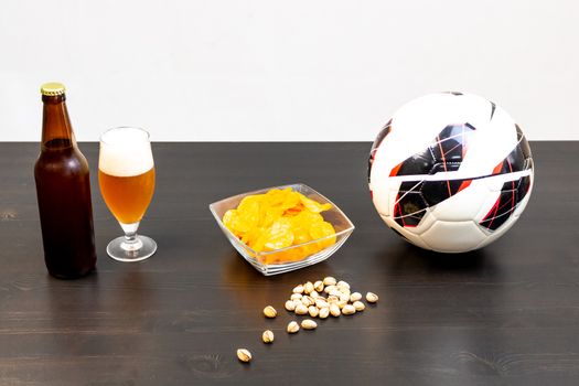 People prepared to watch football on TV with beer. There's beer on the table, ball, TV remote, snacks. Craft beer. Light background.