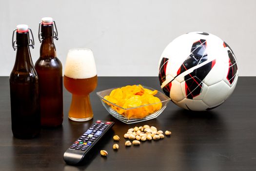 People prepared to watch football on TV with beer. There's beer on the table, ball, TV remote, snacks. Craft beer. Light background.