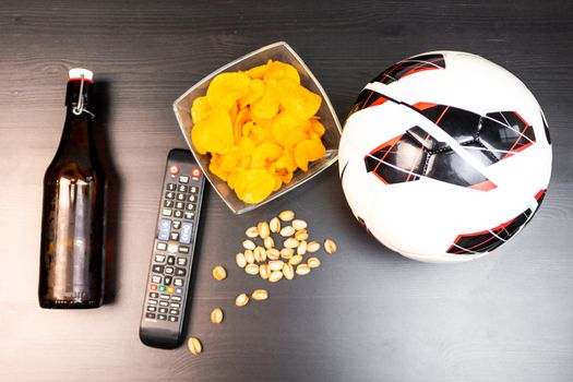 People prepared to watch football on TV with beer. There's beer on the table, ball, TV remote, snacks. Craft beer. Light background. The view from the top.