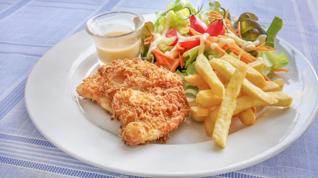 Deep fried fish steak served with french fries and fresh vegetables on white plate