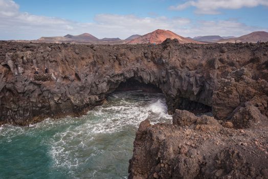 Lanzarote landscape. Los Hervideros coastline, lava caves, cliffs and wavy ocean. Unidentifiable tourist are in the background