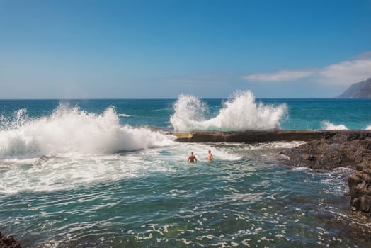 Unidentifiable Tourist swimming in coastline landscape in Puerto Santiago, Tenerife, Spain.