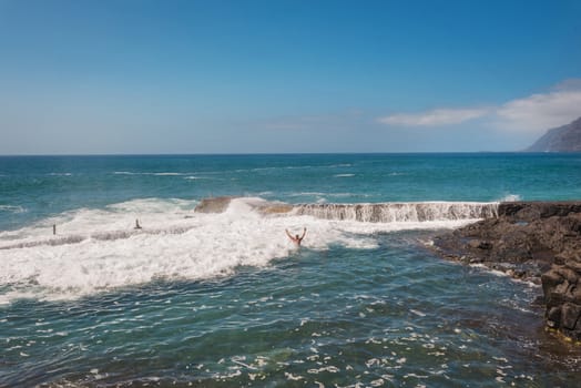 Unidentifiable Tourist swimming in coastline landscape in Puerto Santiago, Tenerife, Spain.