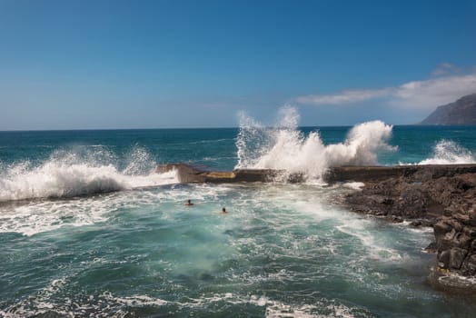 Unidentifiable Tourist swimming in coastline landscape in Puerto Santiago, Tenerife, Spain.