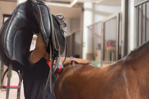 Man saddle a horse in the stall.