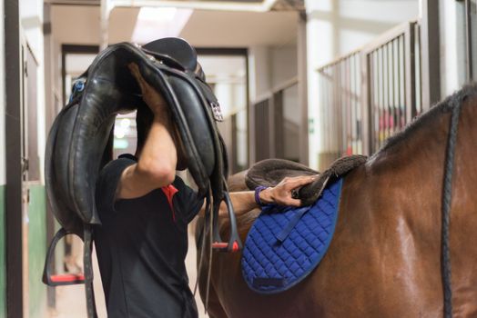 Man saddle a horse in the stall.