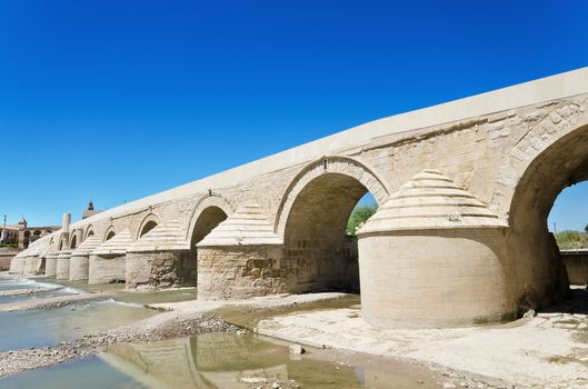 Roman bridge and Guadalquivir river over blue bright sky in Cordoba, Andalusia, Spain.