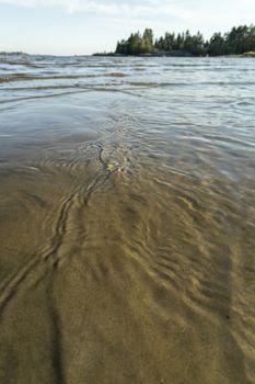 Ripples in Water and Sand in Ocean with trees and clouds.