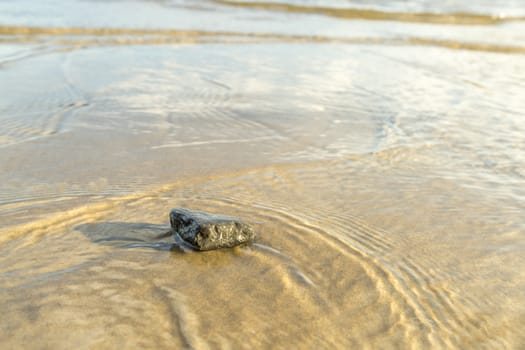 Stone in Sand with Water Ripples close up.