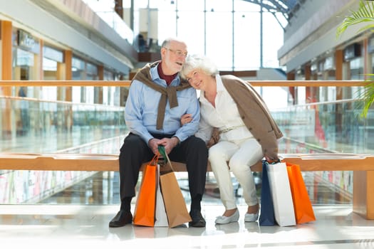 Senior couple sitting in shopping mall with gifts