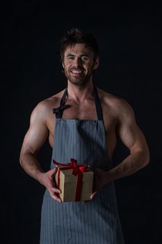 Handsome muscular naked man in an apron holding holiday gift box