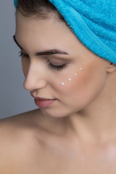 Beautiful woman with towel on head applying creme after shower