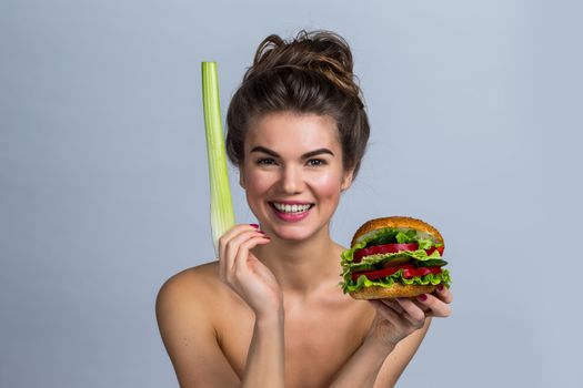 Young woman holding hamburger made of vegetables and stalk of celery, healthy eating concept