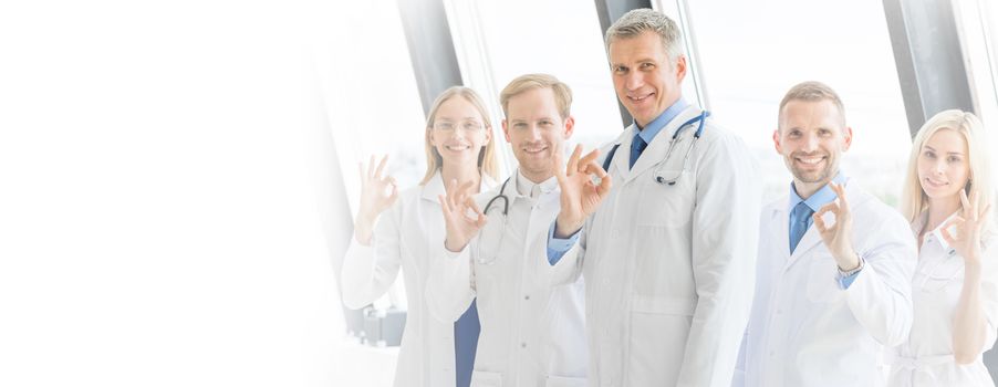 Medical team in hospital showing ok sign, white copy space