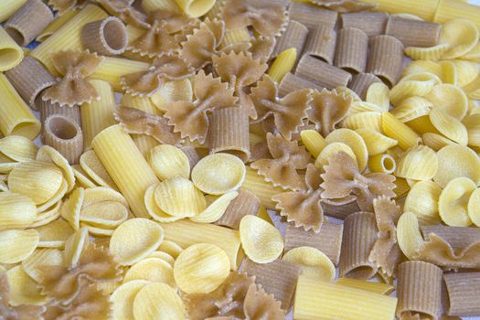 raw assorted wholemeal and normal pasta on a wooden dish