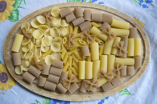 raw assorted wholemeal and normal pasta on a wooden dish