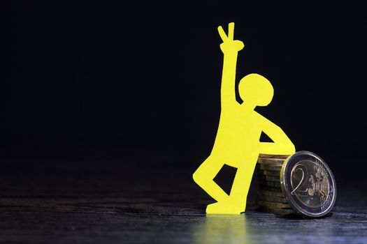 Man made from yellow paper standing near column of coins