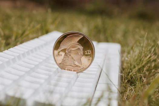 Digital currency physical gold titan bitcoin on white keyboard in grass.