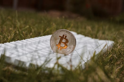 Cryptocurrency physical silver bitcoin coin with yellow sign on white keyboard in garden.