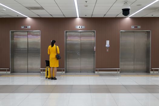 Air hostess with yellow uniform is checking her flight schedule and waiting elevator at the international airport terminal with copy space.