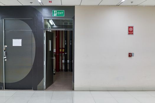 Green warning fire exit on open door for escape from building with fire alarm signal on wall with copy space at the international airport terminal.