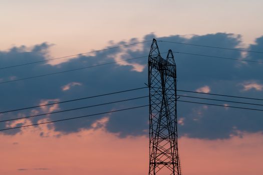 Silhouette of High voltage electric pylon, tower in sunset with clouds on the sky, close up
