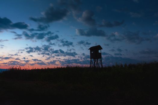 Hunting tower, hide, lookout in dusk with cloudscape, corn field in front
