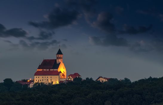 Illuminated Christian Church on hill at dusk, Ptujska Gora, Slovenia with clouds and fog in the sky as background