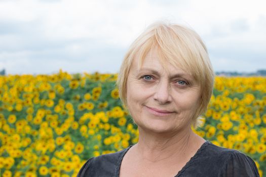 Headshot portrait of smiling aged retired blond white woman with direct sight of green blue eyes looking into camera