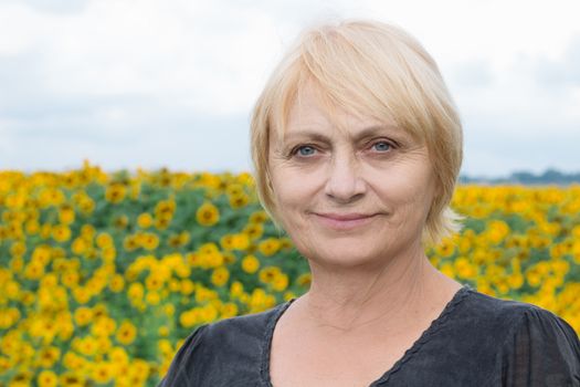 Headshot portrait of smiling aged retired blond white woman with direct sight of green blue eyes looking into camera