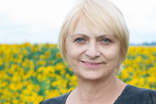 Headshot portrait of smiling aged retired blond white woman with direct sight of green blue eyes looking into camera