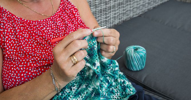 woman engaged in crocheting a sweater of blue wool