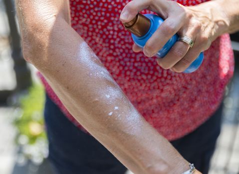 adult woman holding bottle of sunscreen lotion before applying, close up of hands