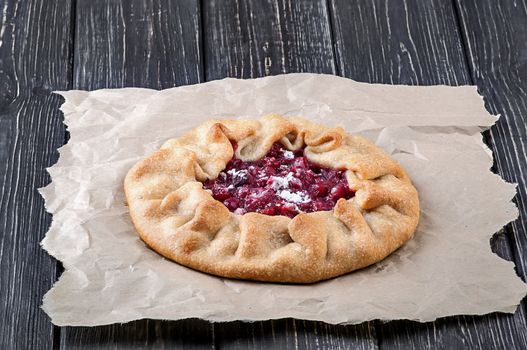 Open pie Galette with red gooseberry on crumpled paper and wooden table
