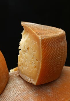 Cut slice block section of old aged matured hard artisan cheese over black background, close up, low angle view