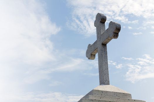 Christian stone cross on the Blue Sky with clouds.