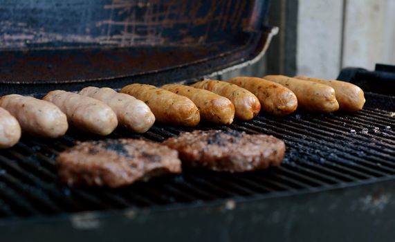 Beefburgers and sausages cooking on an open barbecue grill