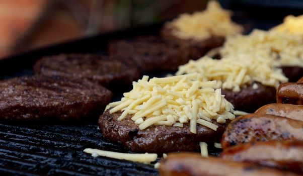 Grated cheese piled on top of a barbecued hamburger on a hot grill