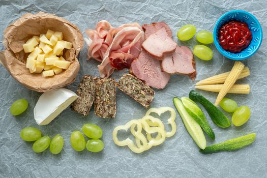 Cold appetizer. Cold cuts. Different snacks on a white crumpled paper, bacon, fruits, grapes, vegetables, from above.