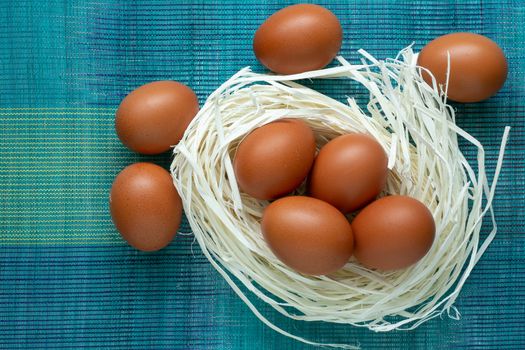 Eggs lie on the decor in the form of a nest. Eggs lie in an artificial nest on a blue background